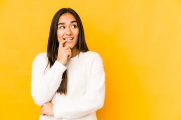 Young woman isolated on a yellow background relaxed thinking about something looking at a copy space.