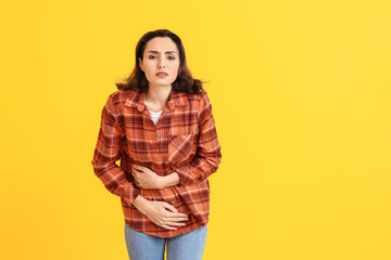 Young woman suffering from menstrual cramps on color background