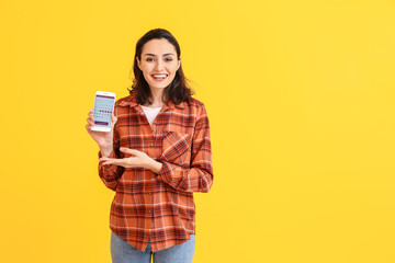 Young woman with menstrual calendar on mobile phone screen against color background