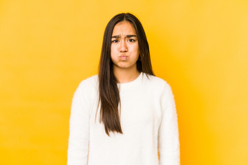 Fototapeta premium Young woman isolated on a yellow background blows cheeks, has tired expression. Facial expression concept.