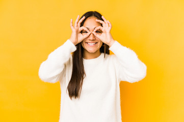 Young woman isolated on a yellow background showing okay sign over eyes