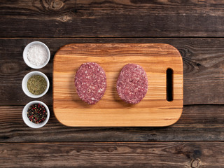 Raw meat cutlets for hamburgers on wooden cutting board. Flat lay.