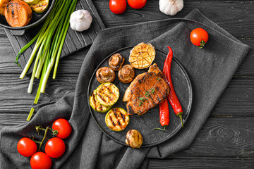 Plate with cooked pork steak and vegetables on table