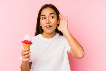 Young asian woman holding a ice cream isolated trying to listening a gossip.