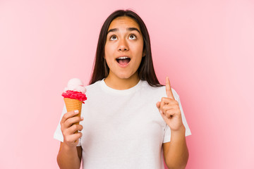 Young asian woman holding a ice cream isolated pointing upside with opened mouth.