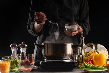 The chef cooks, sprinkling salt in a boiling pan, frozen in motion. Against the background of vegetables. Cooking and gastronomy, recipe book and food.