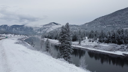 Fototapeta premium Large river cutting through snow covered valley with tree mountain range and curving roads