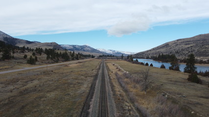 Rail road track as a leading line through a grass valley surrounded by tree covered rolling hills and a snow covered mountain range