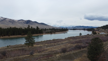 Fototapeta premium Large river winding through a valley with rolling grass hills and snow covered mountains in the distance