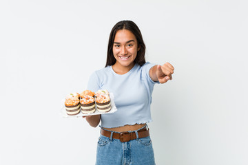 Young mixed race indian holding a sweet cakes cheerful smiles pointing to front.