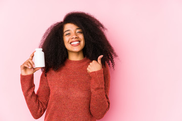 Young afro woman holding a vitamins isolated Young afro woman holding a vitaminssmiling and raising thumb up