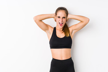 Fototapeta na wymiar Young caucasian fitness woman posing in a white background covering ears with hands trying not to hear too loud sound.