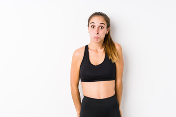 Young caucasian fitness woman posing in a white background shrugs shoulders and open eyes confused.