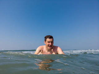 Male in the sea near the coast. Attractive man in sea splashing water and posing to camera. Smiling man having fun in sea water.