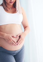 happy pregnant woman placing hands on belly in heart symbol