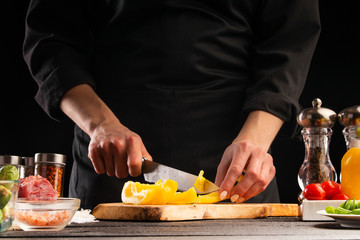 Chef gotomit salad, slicing peppers on a background with vegetables. Ingredients for cooking. Restaurant business, cooking, tasty and healthy nutrition.