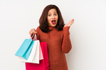 Middle age latin woman holding a shopping bags isolated surprised and shocked.