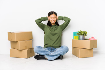 Young chinese woman moving to a new home covering ears with hands trying not to hear too loud sound.