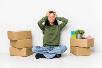 Young chinese woman moving to a new home laughs joyfully keeping hands on head. Happiness concept.