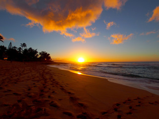 Beautiful Sunset over the ocean and beach with waves moving to shore and foot prints in the sand