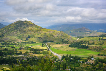 Arrow Junction Lookout point, a mountain viewpoint overlooking mountains and villages. In the summer, there are wild flowers and green fields at Crown Range Road, Otago, New Zealand.