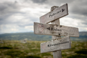 policies, rules and requirements text on wooden road sign outdoors in nature. - obrazy, fototapety, plakaty