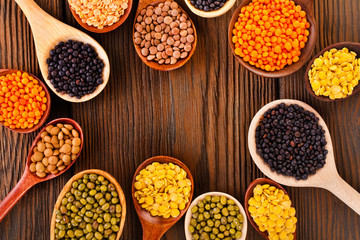 Various lentils in the wooden spoons on a wooden background. Top view.