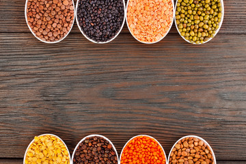 Bowls of various lentils on a wooden background. Top view. Copy space.