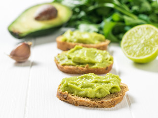 Freshly prepared guacamole on slices of bread on a white wooden table. Diet vegetarian Mexican food avocado.
