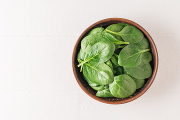 A clay bowl with spinach leaves on a white wooden table. Food for fitness. The view from the top.
