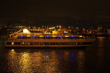 Fototapeta na wymiar Night pleasure boat, or yacht for a walk with people. Night city with a river and a big boat