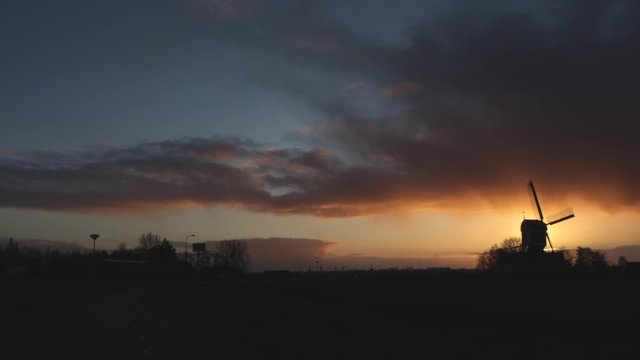Traffic driving past old windmill at sunset in the Netherlands