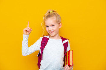 Back to school. Portrait of blonde school girl with bag and books. Pointing finger up. Yellow...