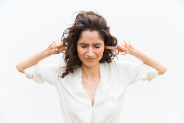 Annoyed young woman plugged ears with fingers. Angry lady with closed eyes posing in studio....