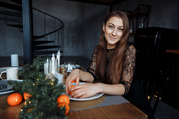 Brunette in a black dress cleans an orange in a beautiful New Year setting