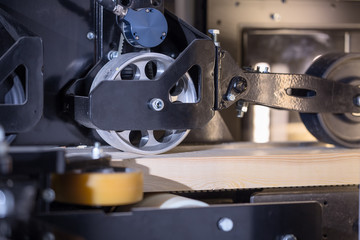 A metal roller presses the board in the machine. Wooden board in a machine tool.