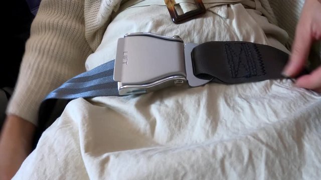 4K, Woman hands fastening seat belt on plane. Passengers sitting inside airplane wearing a safety belt while waiting for takeoff. Safe travel is importance while traveling on plane flight trip-Dan