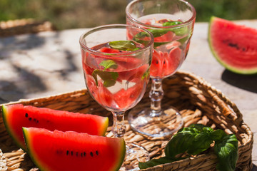 On a table in the garden in a basket are two glasses of lemonade and sliced of watermelon