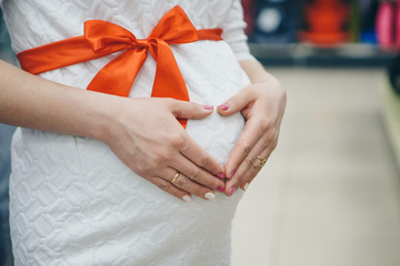 Heart symbol folded from the hands. a pregnant woman is stroking her stomach. Copy space. Healthy lifestyle concept, IVF, mother's day, international women's day, Valentine's day