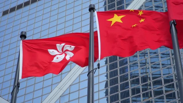 Hong Kong Flag Waving Next to China Flag with Modern Office Building in the Background
