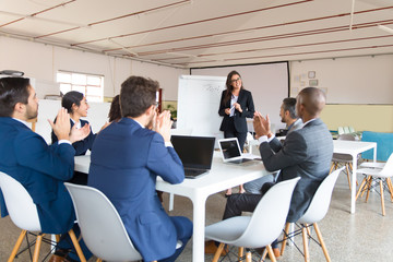 Colleagues applauding after presentation. Smiling office employee standing near whiteboard. Business meeting concept