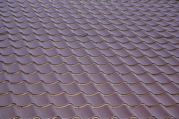 Close up of brown steel roof. Dark steel tiled roof background, Europe. View of a new house. Construction of a new residential private house on blue sky background.