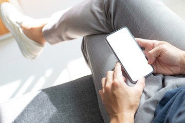 Mockup image blank white screen cell phone.man hand holding texting using mobile on sofa at coffee shop.background empty space for advertise text.people contact marketing business,technology