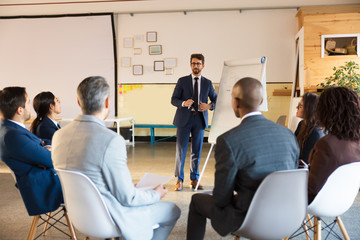 Smiling business trainer working with employees. Group of workers sitting on chairs and listening speaker. Business meeting concept