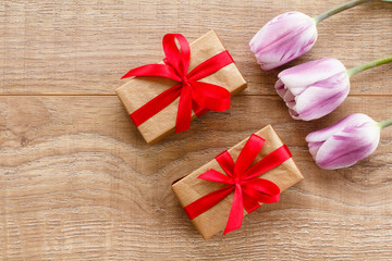 Gift boxes with red ribbons and tulips on wooden boards.