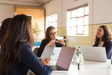 Smiling business team during morning meeting. Cheerful colleagues sitting at table with laptops and talking. Business, teamwork concept