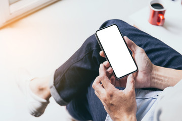 Mockup image blank white screen cell phone.man hand holding texting using mobile on sofa at coffee shop.background empty space for advertise text.people contact marketing business,technology
