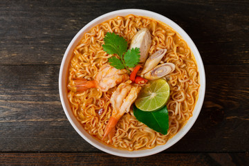 Noodle in spicy soup with shrimp and mushroom in white bowl on wooden table.