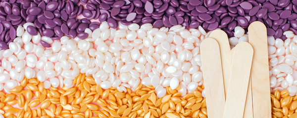 Colorful pearl polymer wax grain seed and wooden spatula stick for depilation closeup. Concept od tools for hair remove, flyer, banner, coupon, discaunt, copy space, spa salon