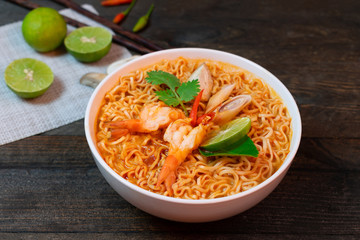 Noodle in spicy soup with shrimp and mushroom in white bowl on wooden table.